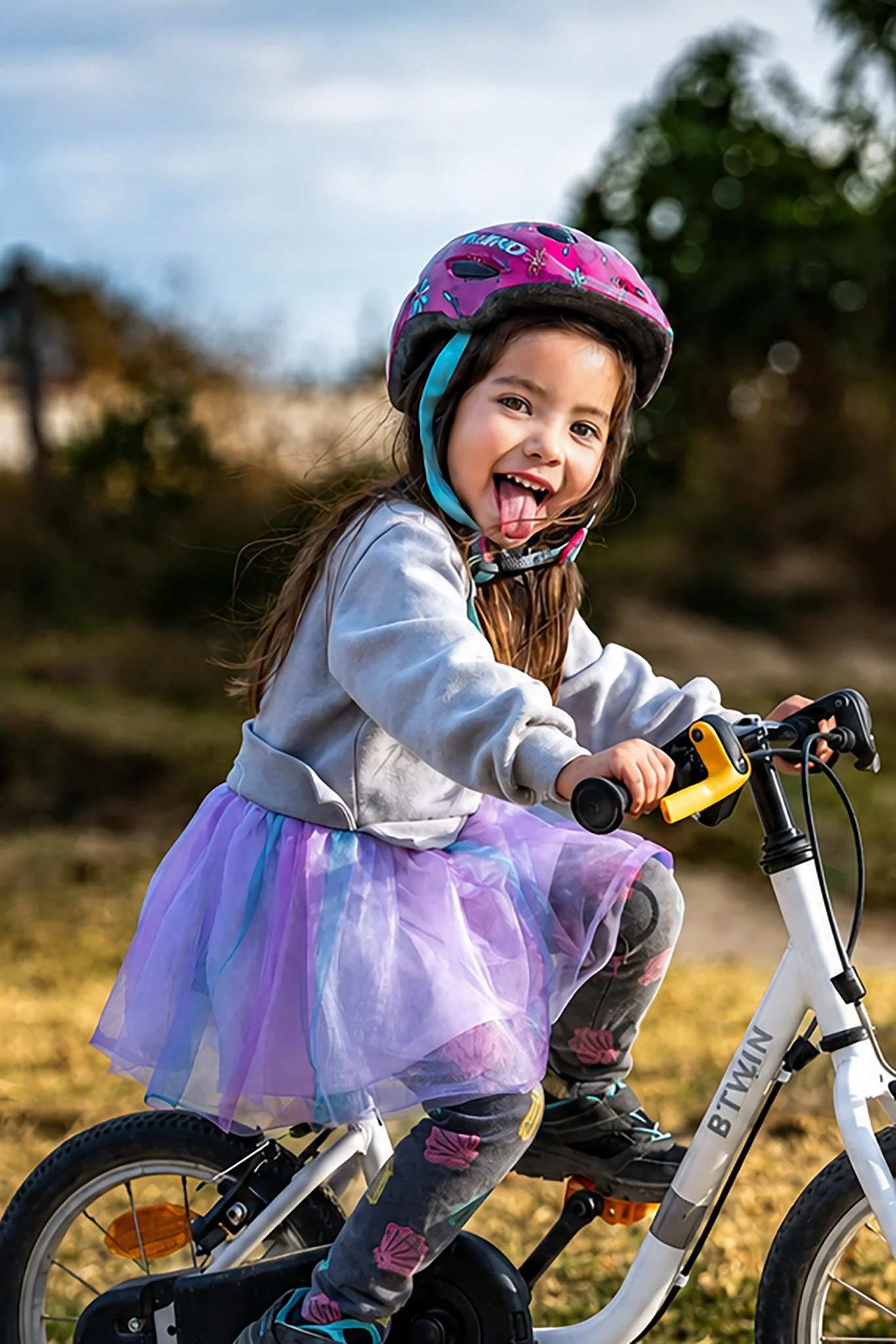 Niña con casco rosa montando bicicleta al aire libre, fotografía deportiva infantil por Carlos Vega.