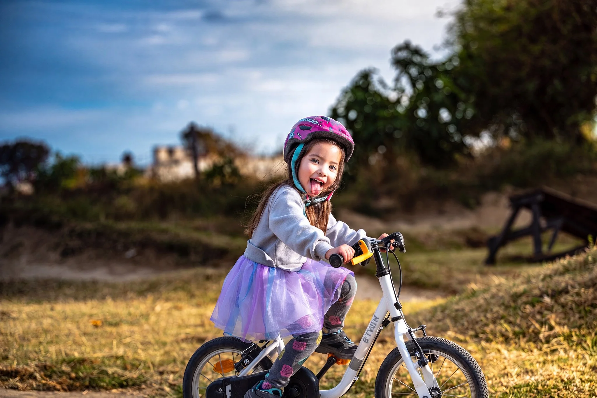 Niña sonriendo mientras monta bicicleta en parque al atardecer, fotografía deportiva infantil por Carlos Vega.