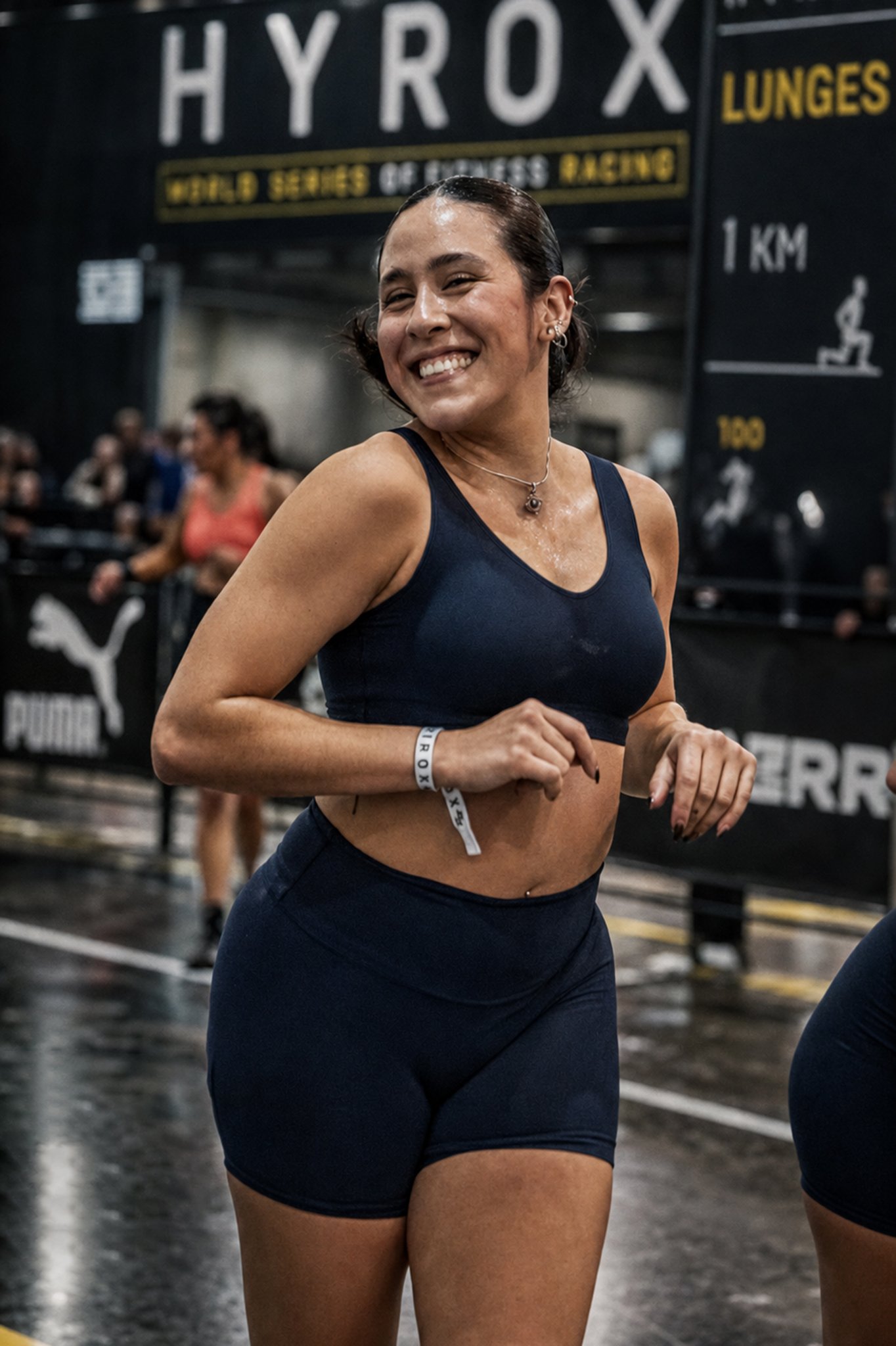 Mujer sonriendo durante carrera indoor en evento fitness, fotografía deportiva por Carlos Vega en Hyrox Puebla.