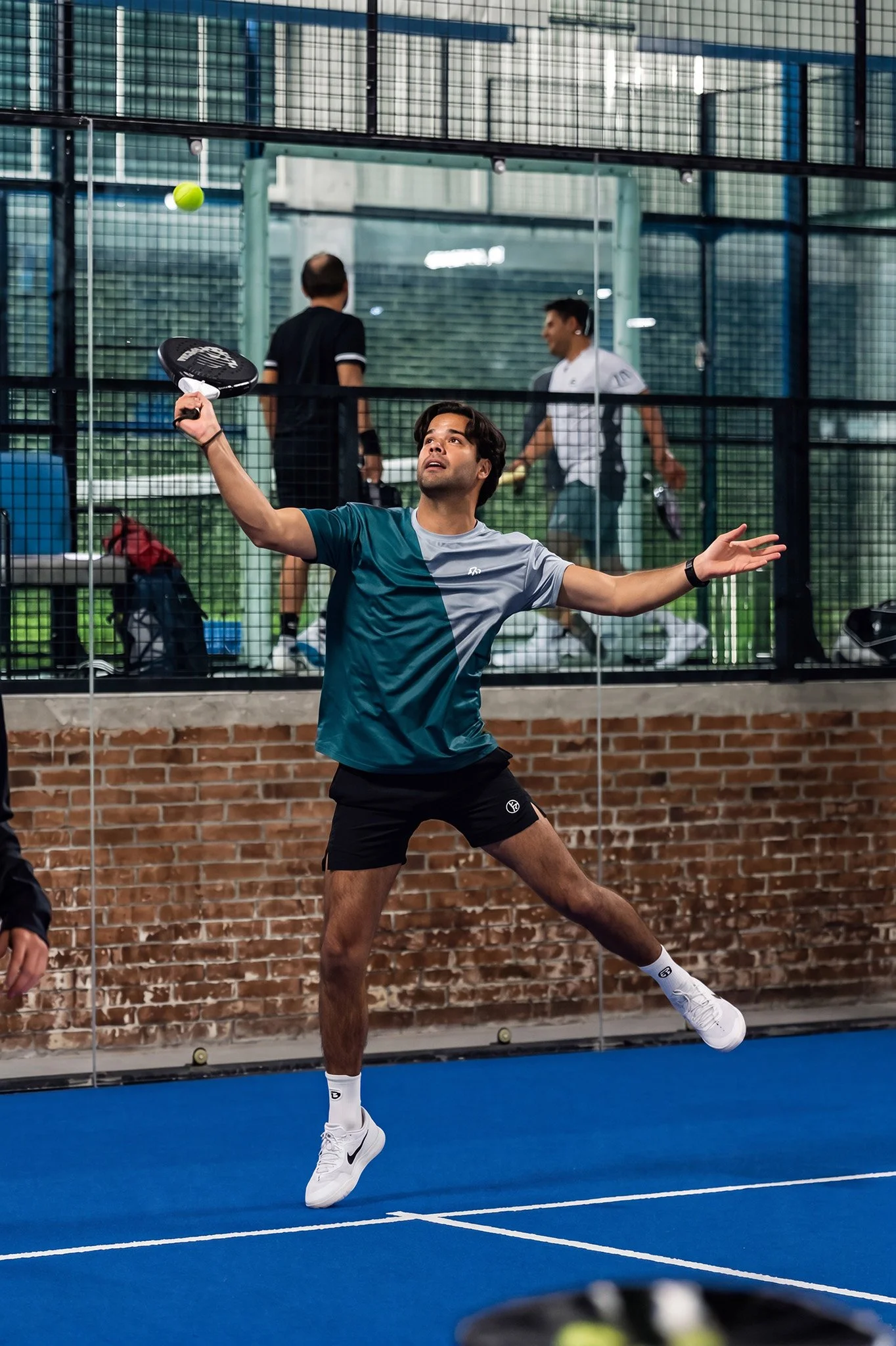 Jugador de tenis realizando saque en cancha cubierta, fotografía deportiva por Carlos Vega.