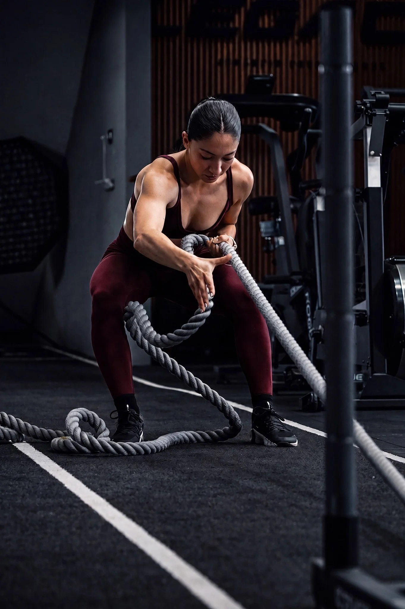 Mujer entrenando con cuerdas de batalla en gimnasio oscuro, fotografía fitness profesional por Carlos Vega en Puebla.