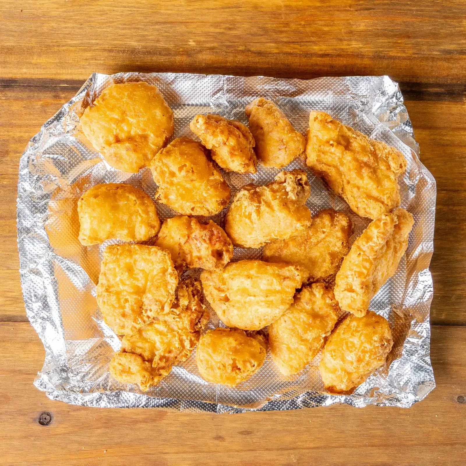 Fried chicken pieces on a sheet of aluminum foil on a wooden surface.