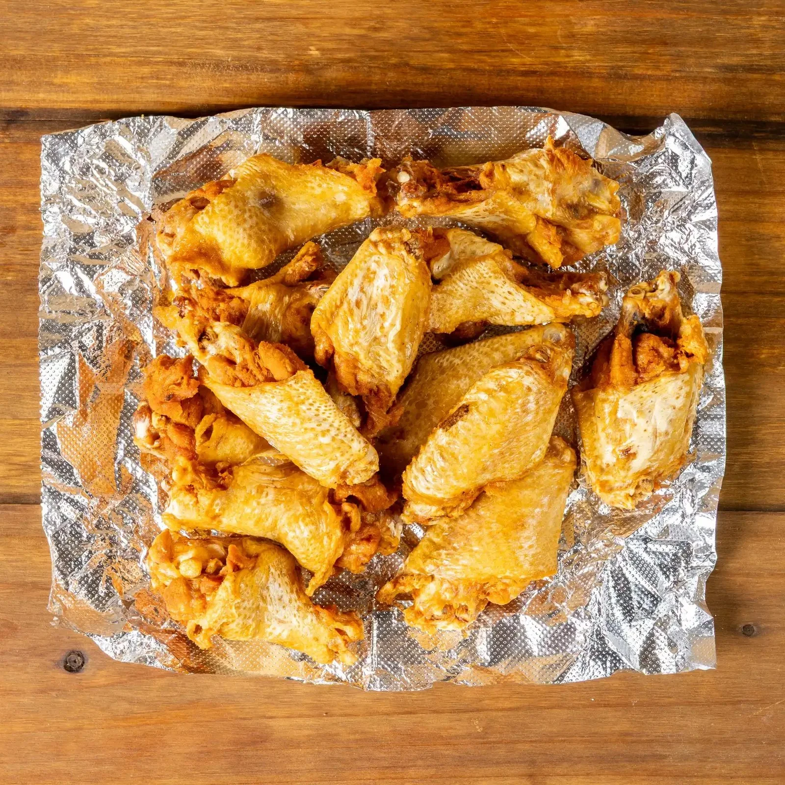 Cooked chicken wings with some pieces of meat and bones on aluminum foil placed on a wooden surface.