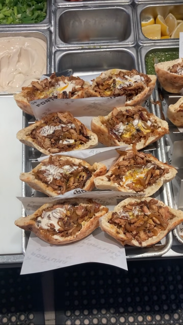 Several chicken shawarma pita sandwiches filled with caramelized onions, and sauces on a metal tray inside a restaurant or kitchen setting.