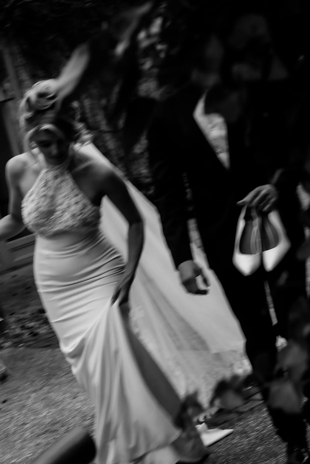 Black and white photo of a woman in a wedding dress and a man in a suit walking together outdoors.