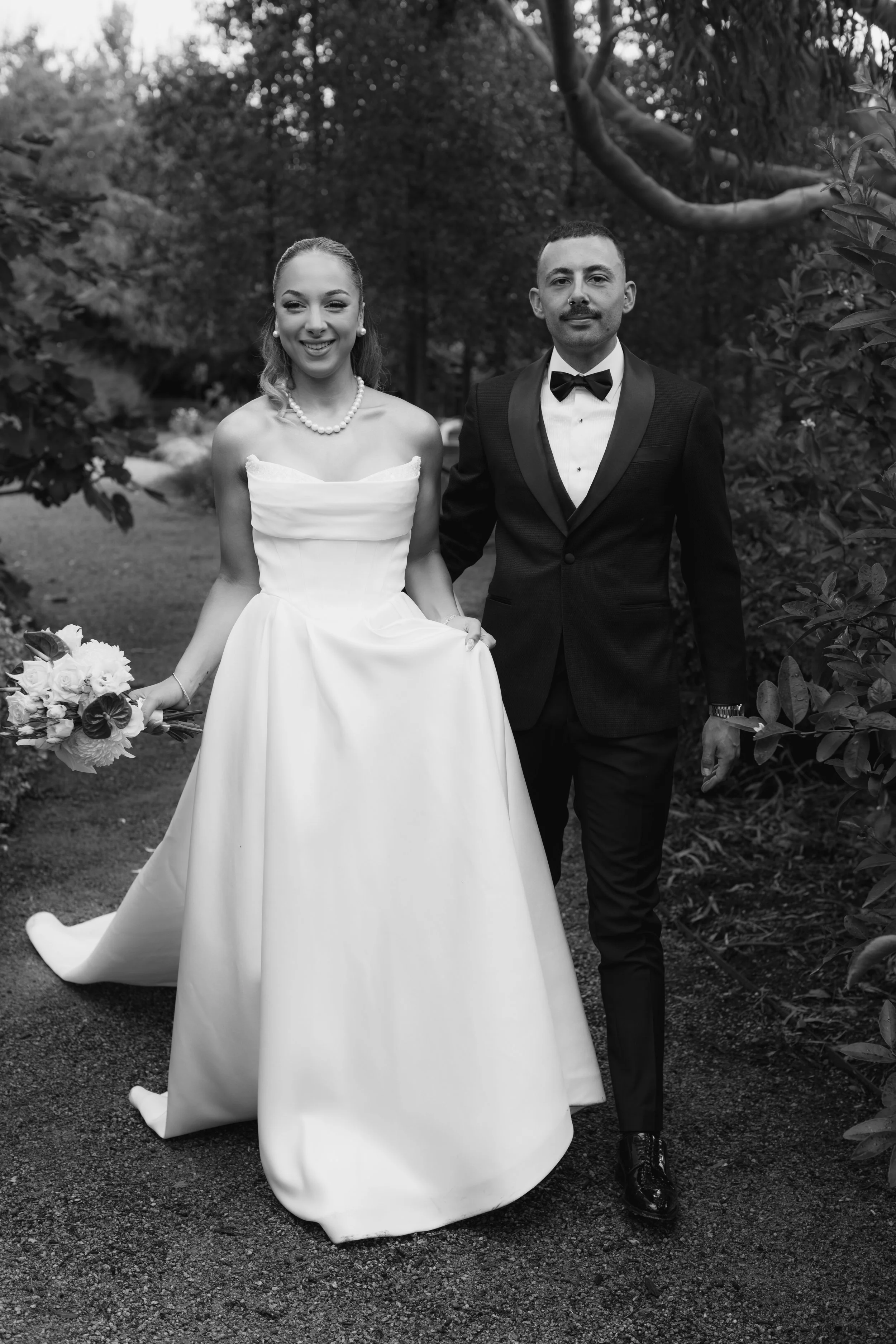 Black and white photo of a bride and groom standing outdoors in a garden.