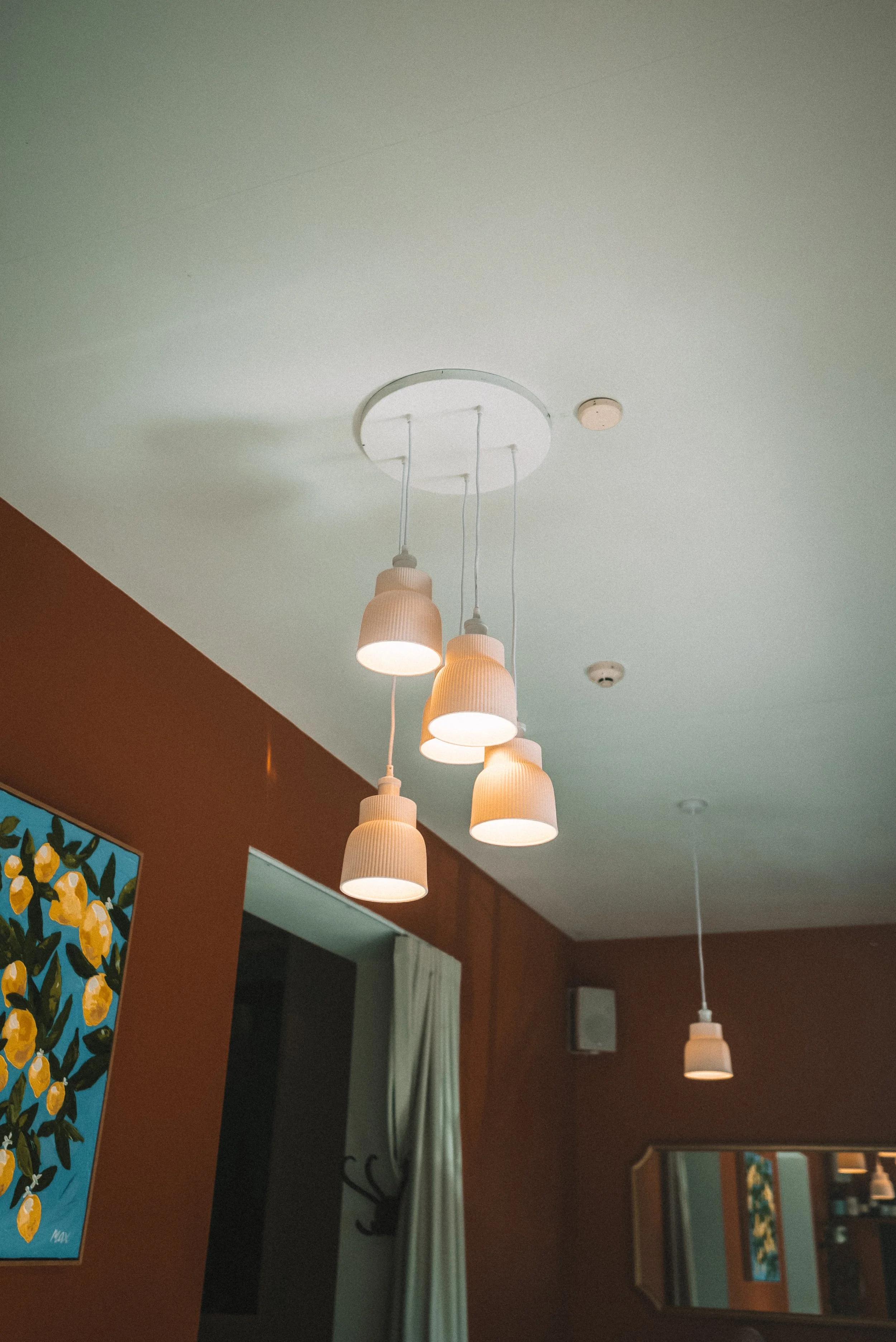 Interior of a room with hanging pendant lights, a teal wall with lemon artwork, and windows with curtains.