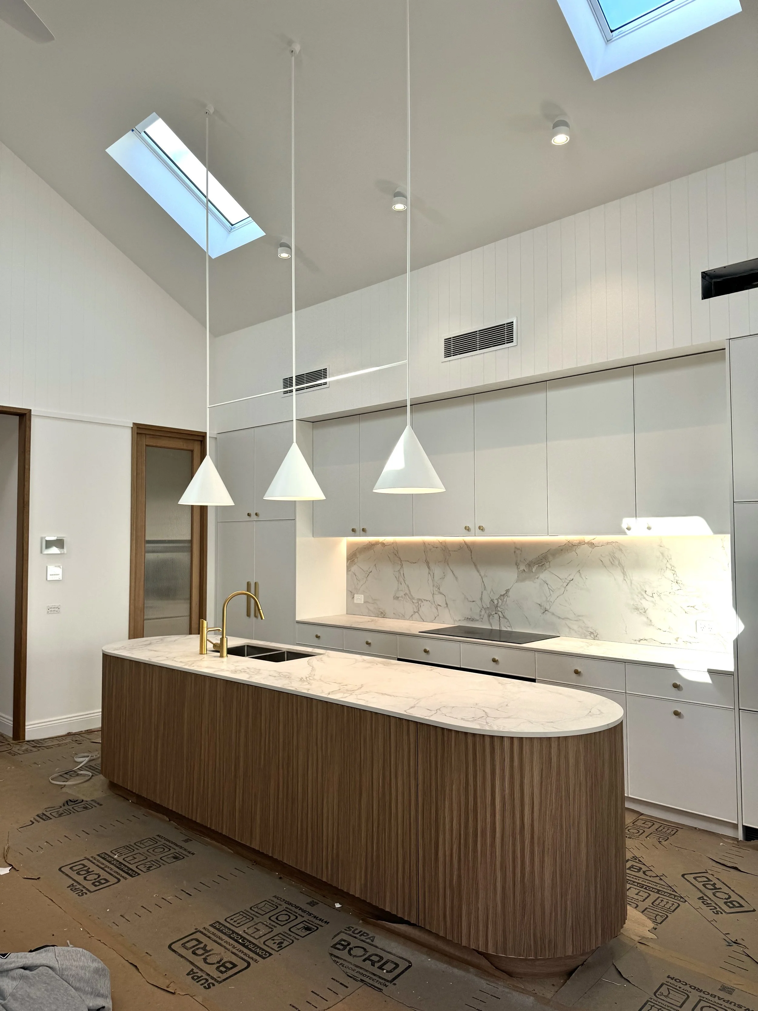 Modern kitchen with island featuring a marble countertop and wooden base, white cabinetry, built-in oven, and purple-gray wall panels. Skylights and recessed lighting illuminate the space.