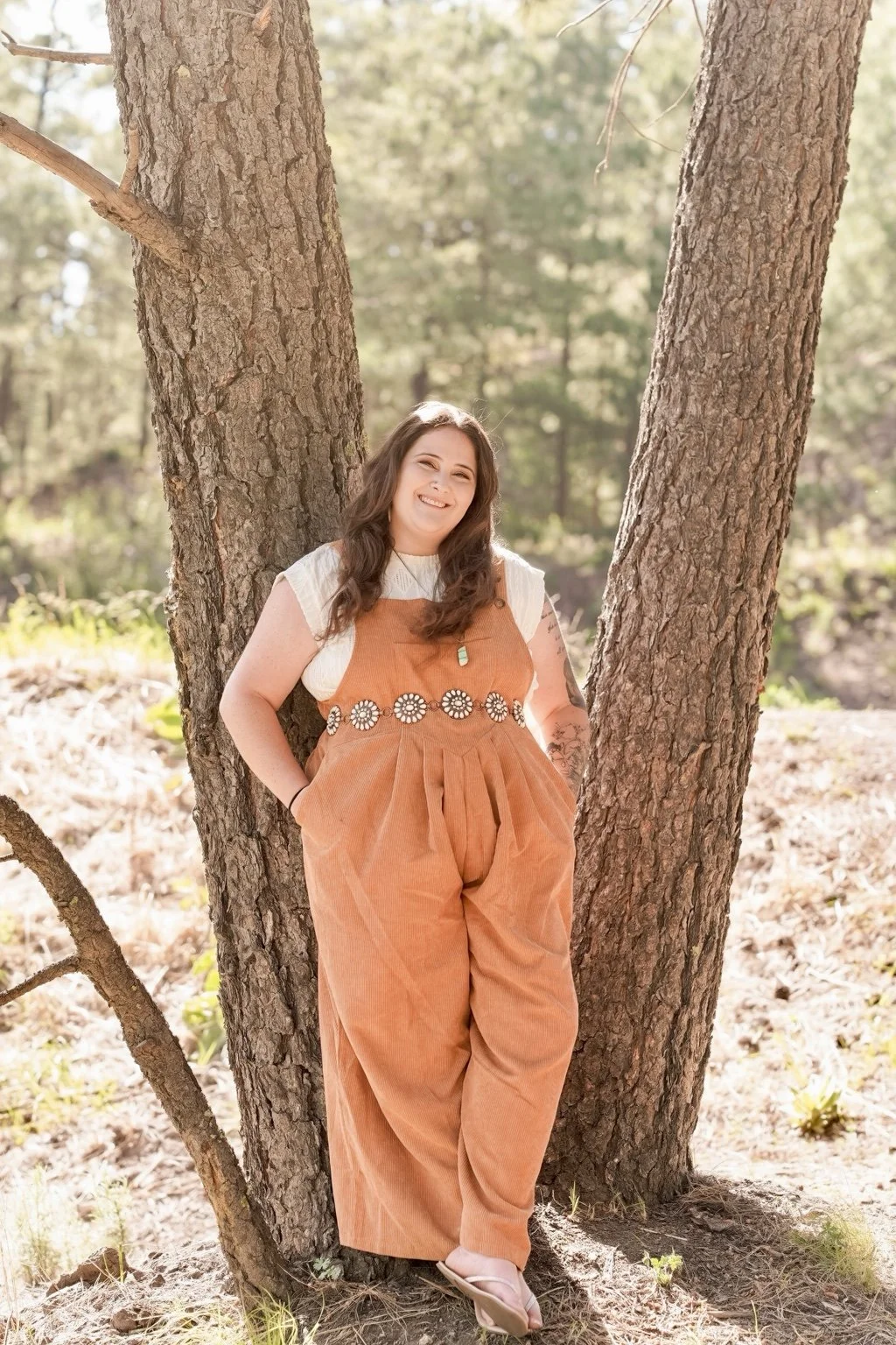 Claire Ramirez-Yocum, therapist at Rooted Pines Healing, standing among pine trees.