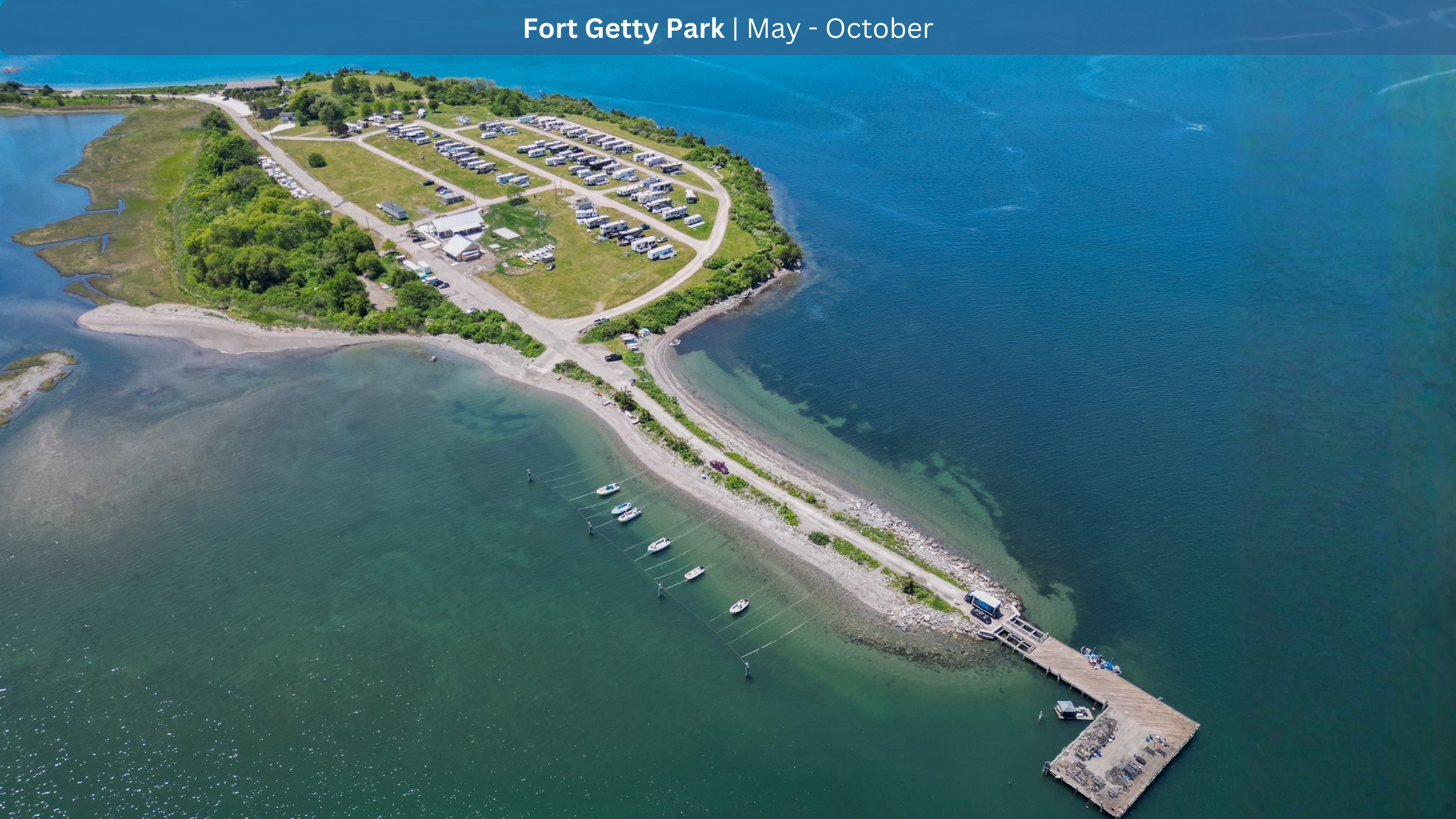 Aerial view of Fort Getty Park showing a parking lot, green landscape, a beach, and boats docked at a pier on a calm body of water, with the ocean in the background.