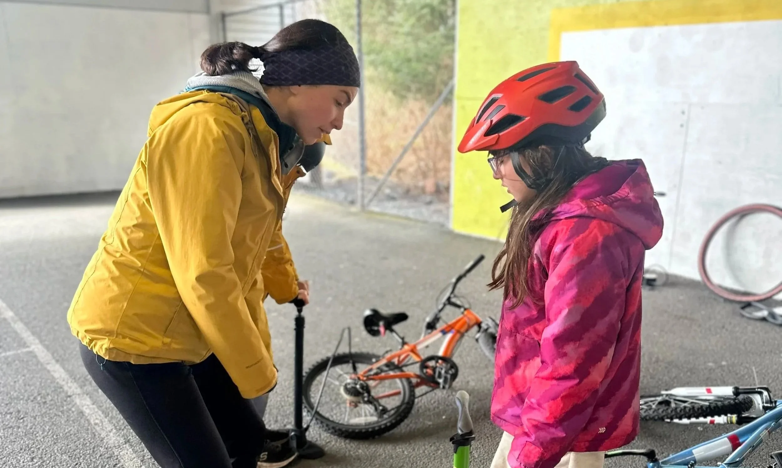 An adult helps a youth pump her bike tires.