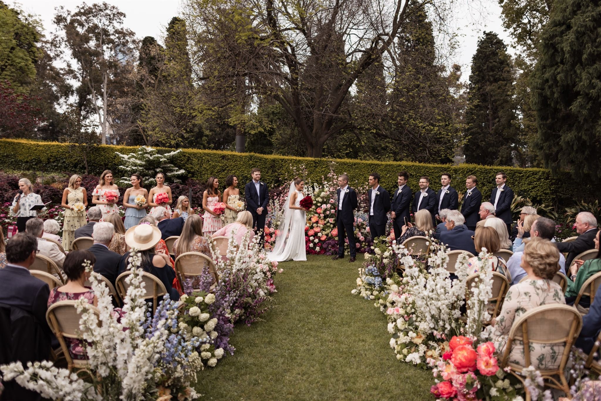 Warm Melbourne wedding ceremony with celebrant guiding couple through vows in a flower-filled garden surrounded by family and friends.
