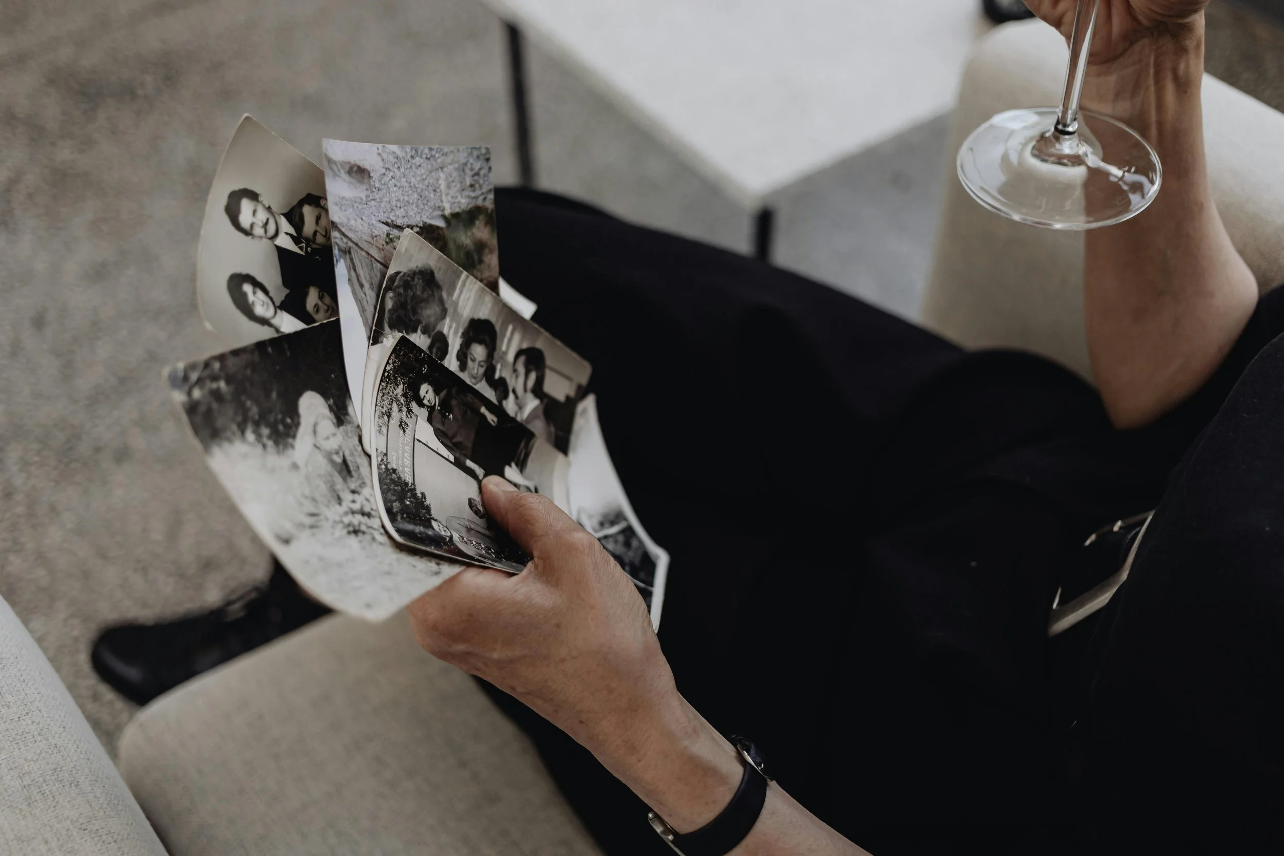 Person holding black and white photographs while sitting with a wine glass
