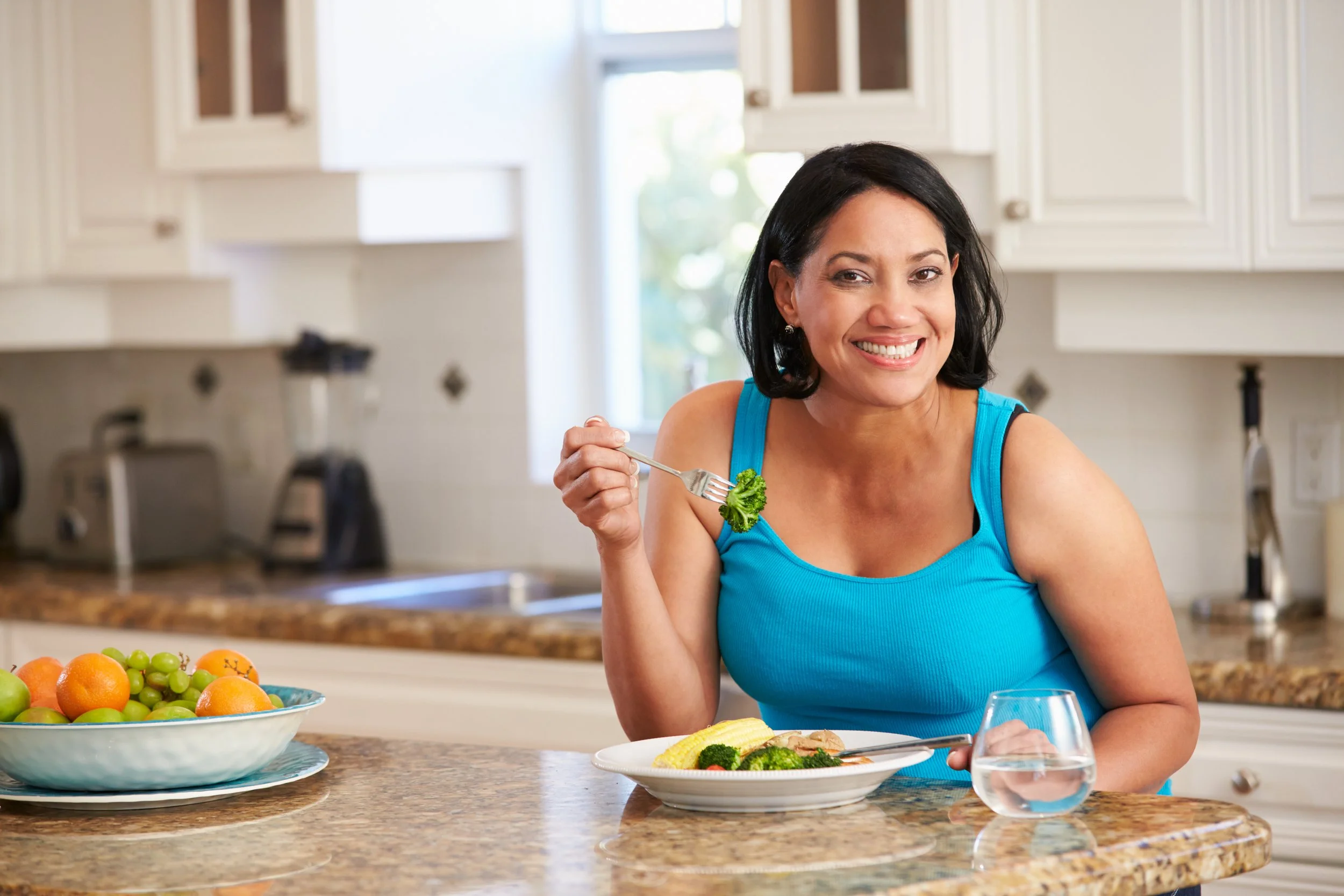 Smiling woman eating a healthy meal of vegetables in her kitchen