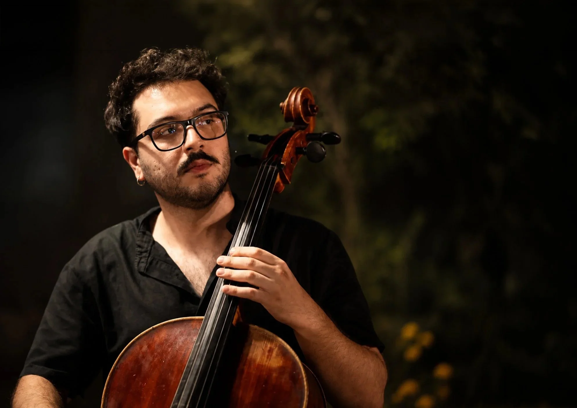 Composer Stefanos Kemanetzis playing the cello outdoors at night.
