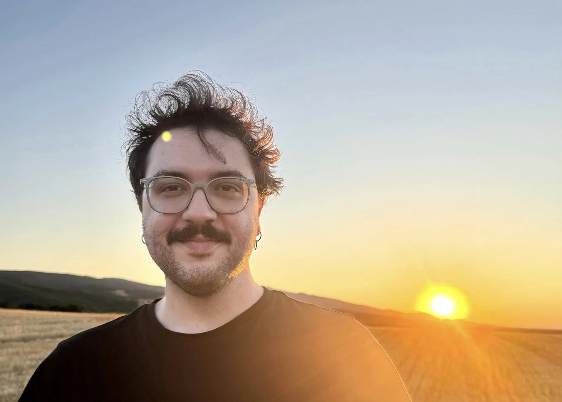 Portrait of composer Stefanos Kemanetzis standing in a field at sunset.