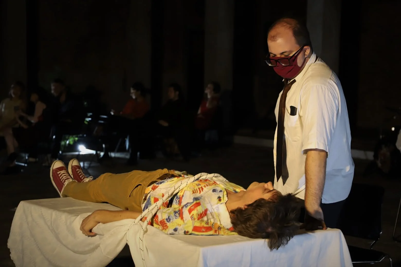 Scene from the operetta ATHANATOS depicting a medical or caregiving scene with a person lying on a table and a man standing beside.