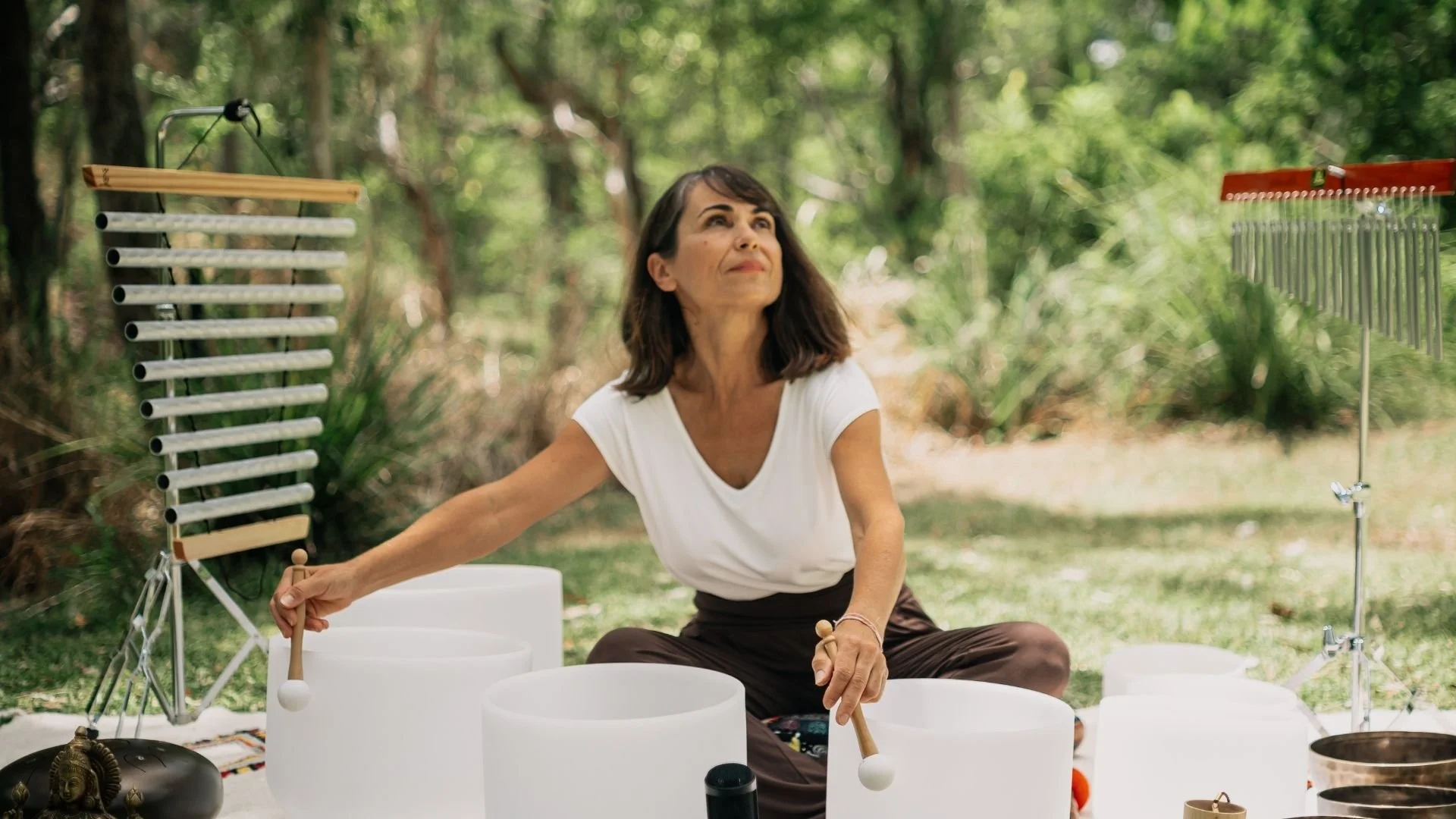 A woman playing crystal singing bowls and other harmonic instruments set in a rainforest.
