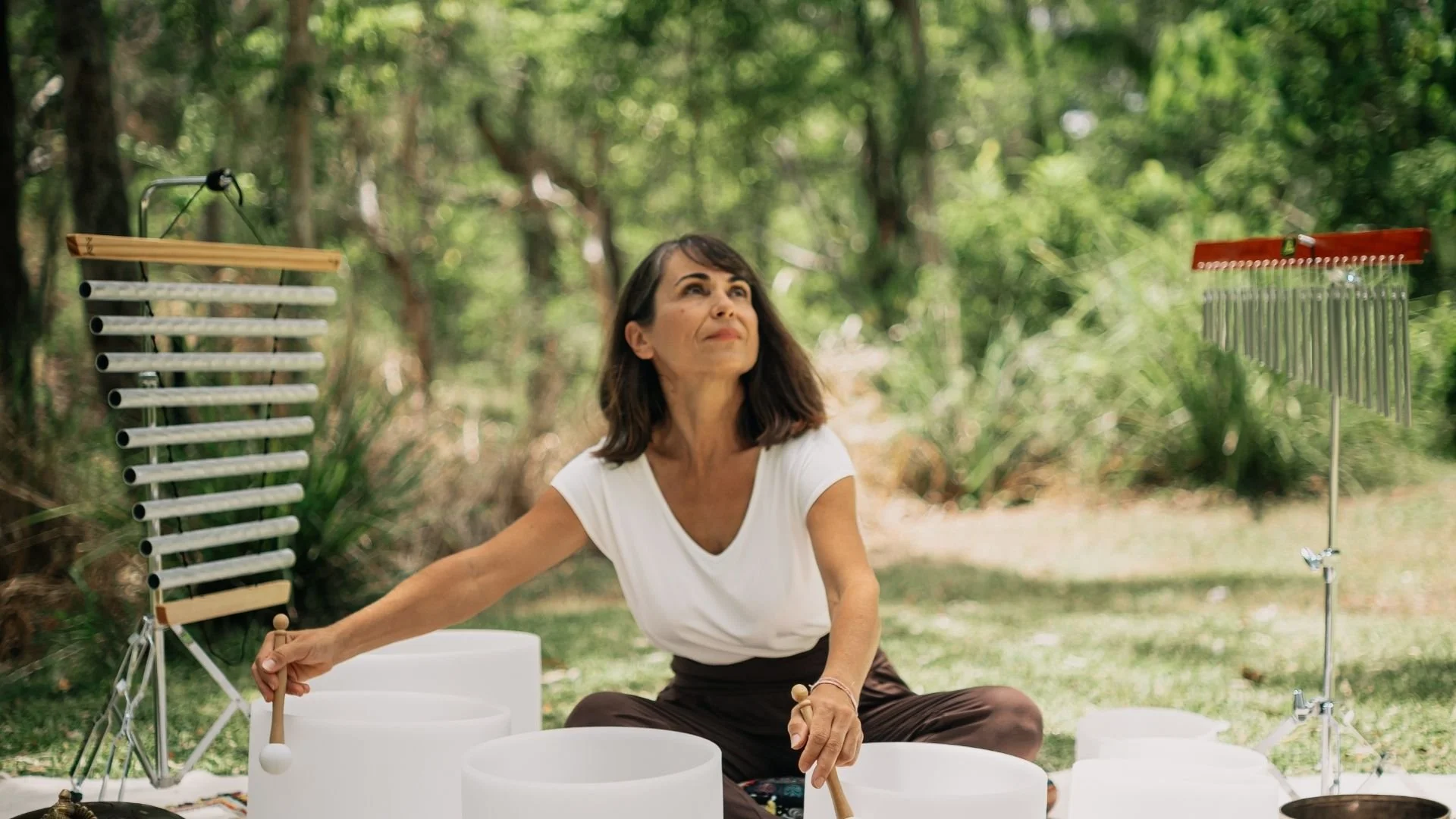 A woman playing crystal singing bowls and other harmonic instruments set in a rainforest.