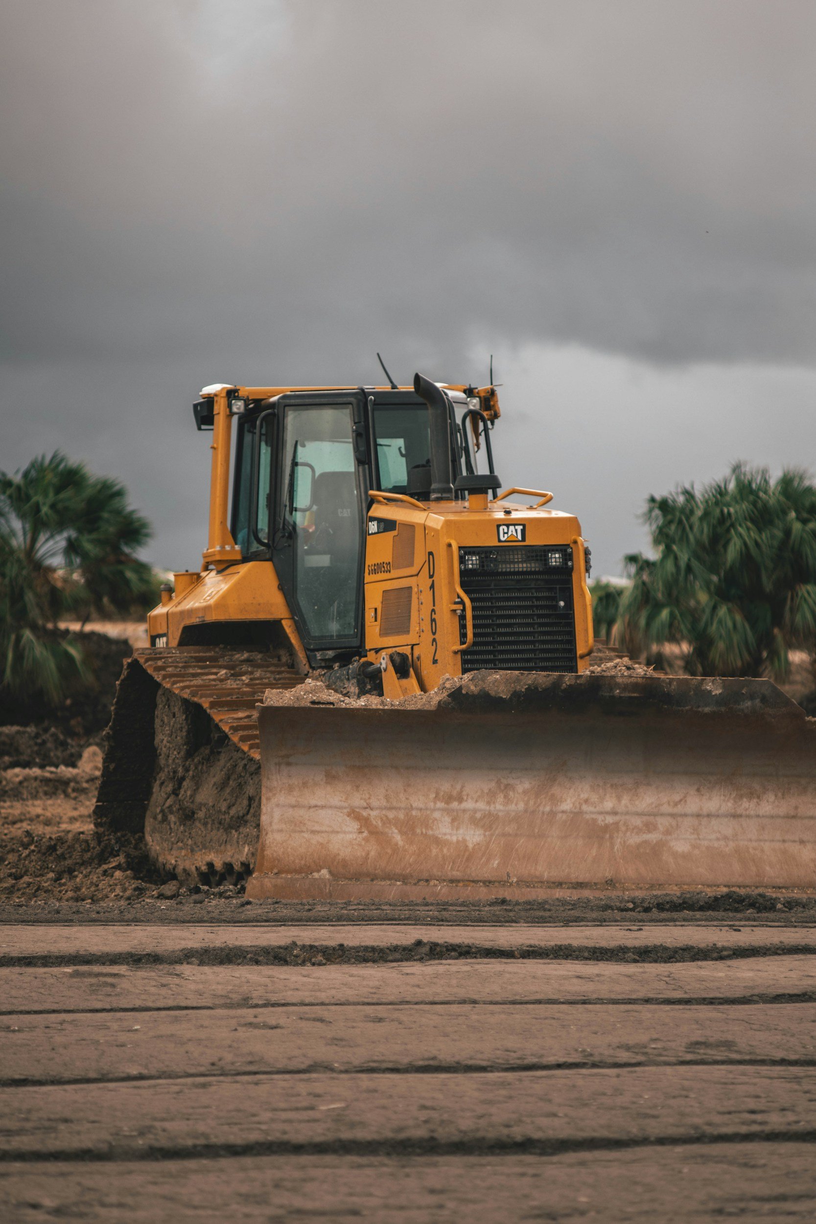 A yellow bulldozer on a construction site with dark storm clouds in the sky.