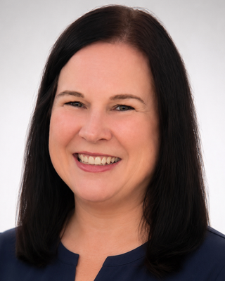 Professional headshot of a smiling woman with long dark hair wearing a navy blouse