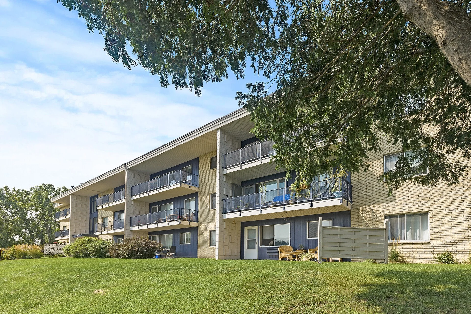 A multi-story apartment building with balconies, surrounded by green grass and trees, under a partly cloudy sky at Imperial Heights in West St. Paul, MN
