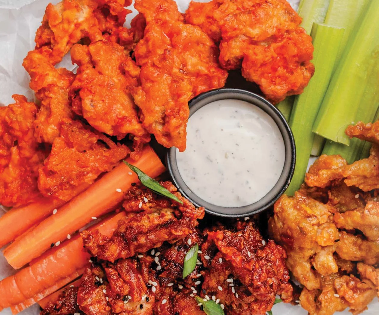 Assorted Asian-fried chicken wings with celery sticks, carrots, and a bowl of ranch dipping sauce.