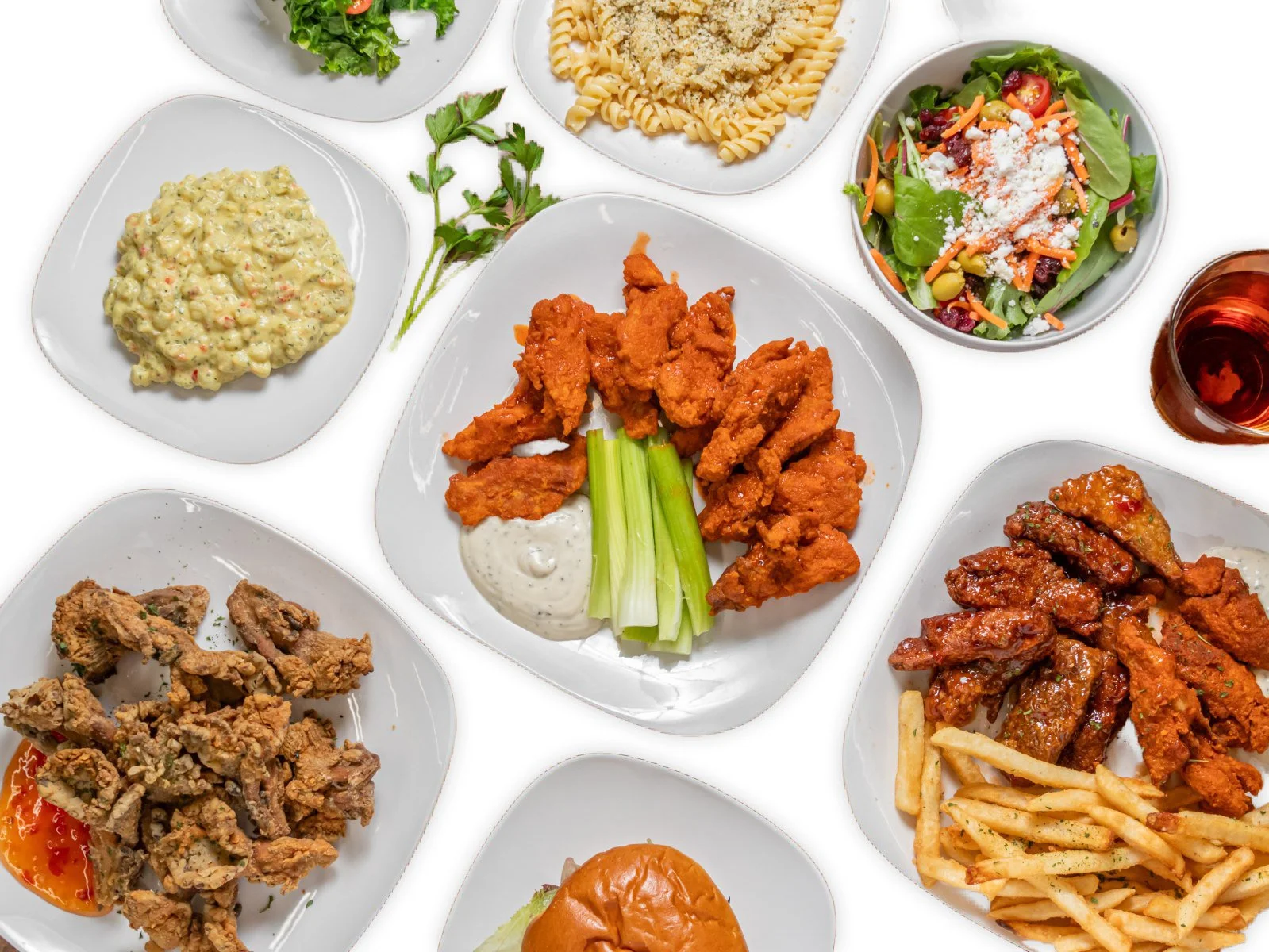 Assorted dishes of fried chicken, pasta salad, macaroni and cheese, vegetable salad, sliders, and French fries on white plates.