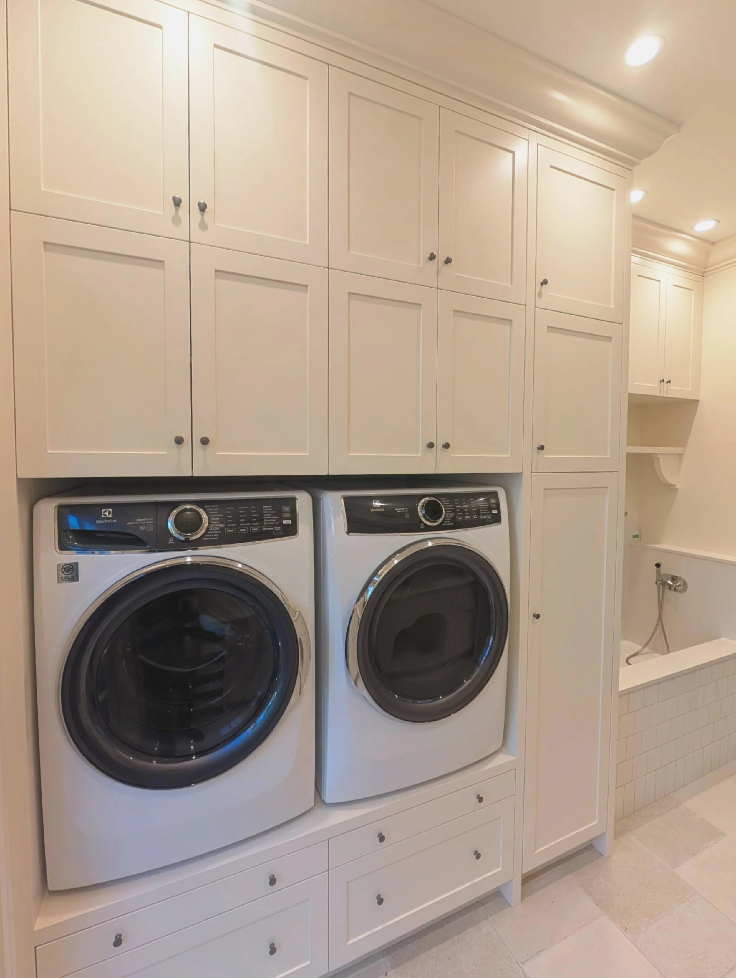 A laundry room with white cabinets above a washer and dryer, and a small utility space with a sink to the right.