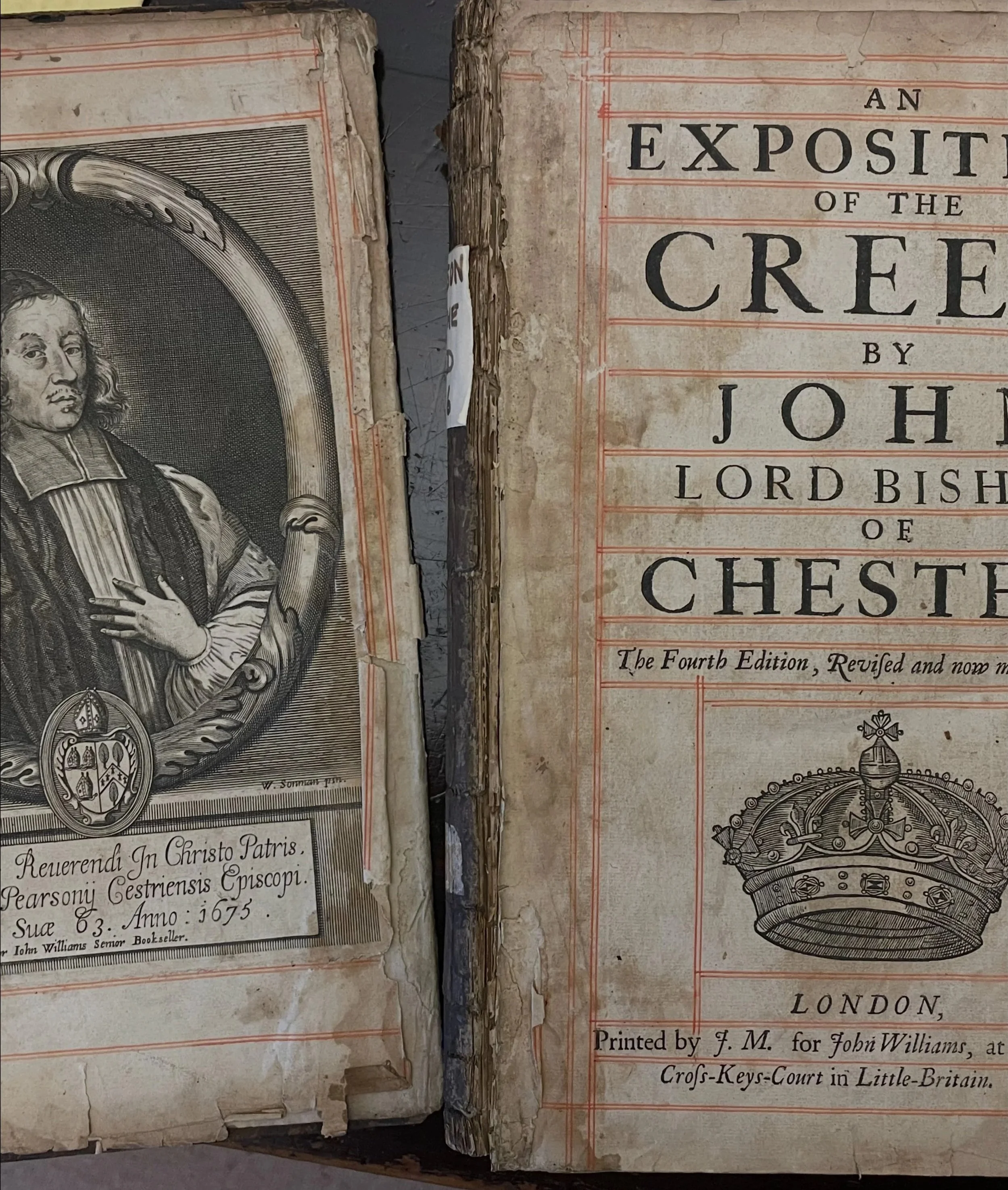 Close-up of old, worn book pages with historical text and illustrations, including a portrait of a man and a crown, with visible tears and damage to the paper.