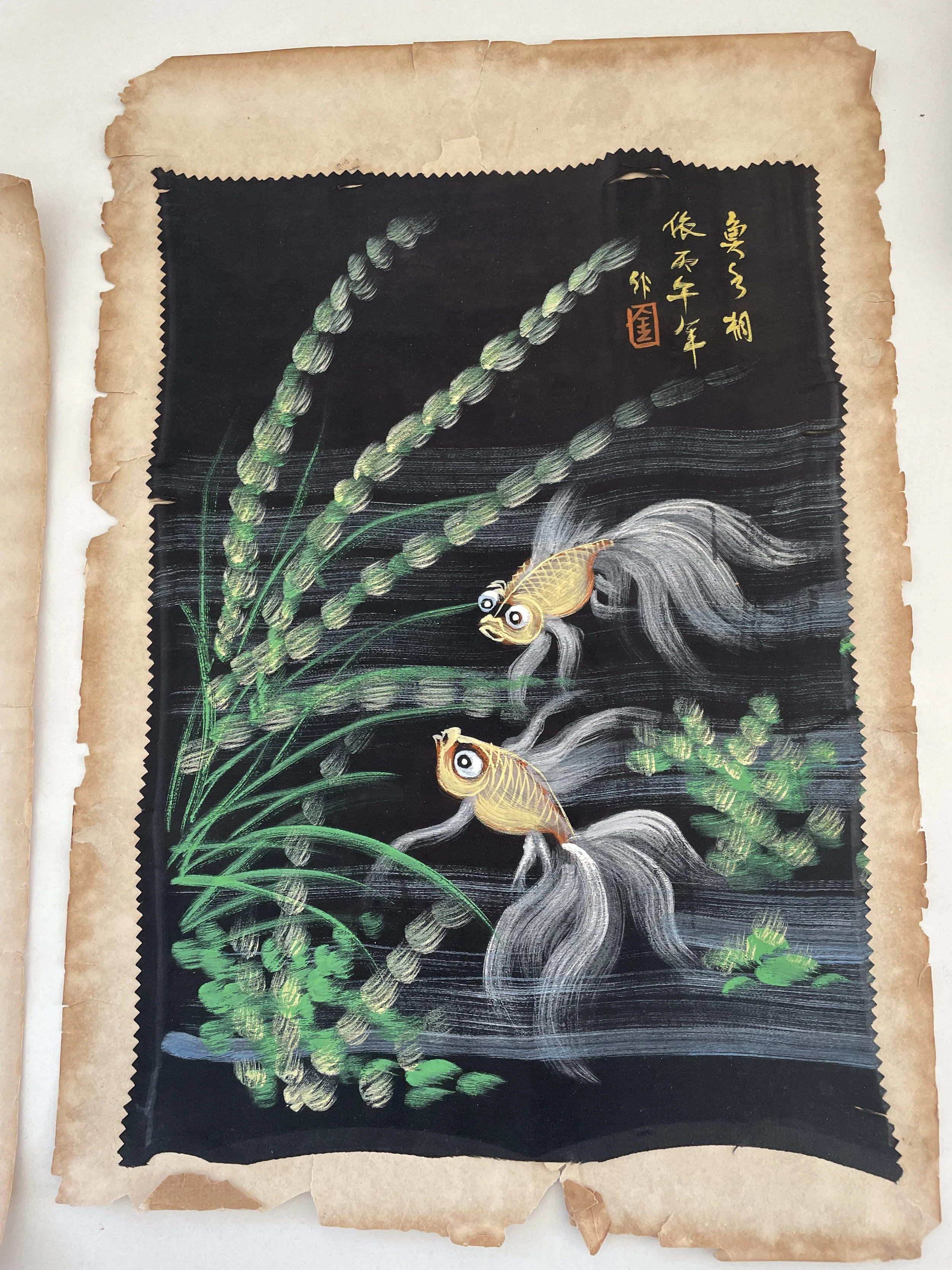 Painting of two koi fish swimming among green plants on a black background, with Japanese characters in gold and red in the upper right corner, and a worn, aged border.