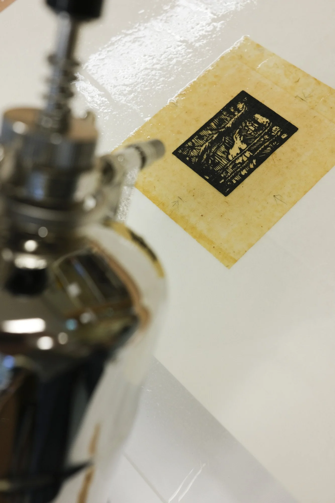 A microscope pointing at a yellowish sample with a black printed pattern on it, placed on a white surface.