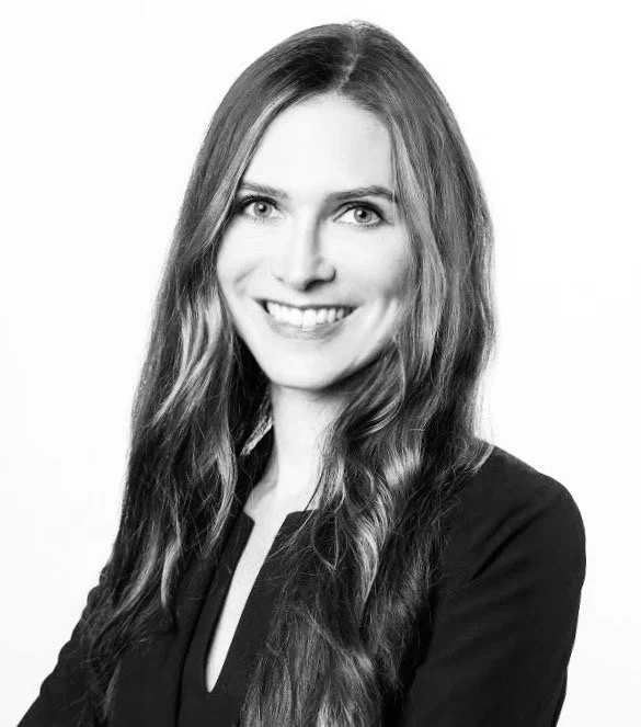 Black and white portrait of a woman smiling with long, wavy hair wearing a blazer.