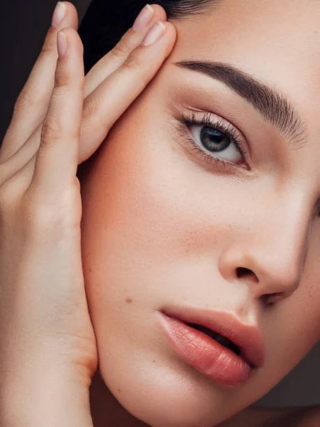 Close-up of a woman's face with her hand touching her temple, showcasing her smooth skin and youthful, blue eye.