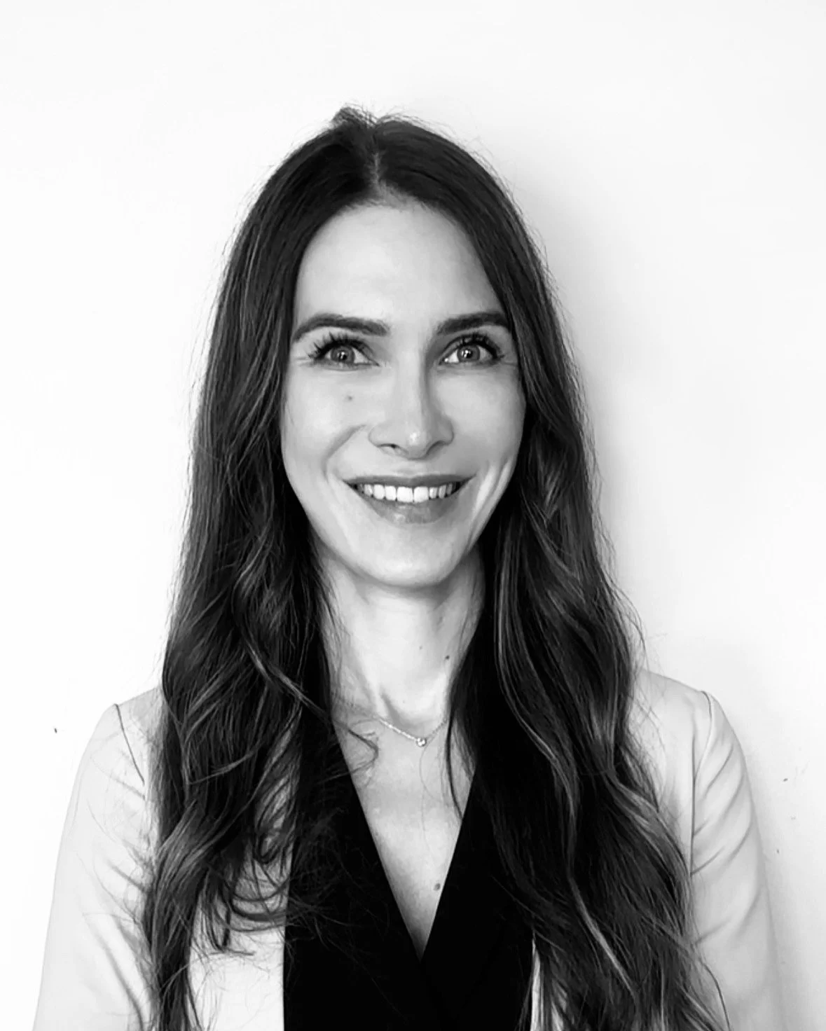 Black and white portrait of a woman with long wavy hair, smiling, against a plain background.