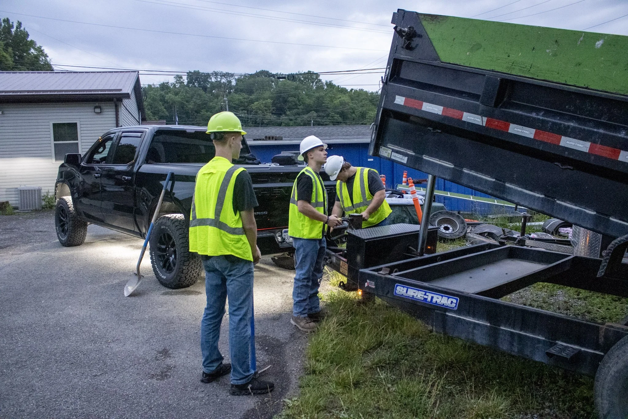 Three Junktion employees in safety vests and hard hats inspecting equipment near a dump truck on a cloudy day.