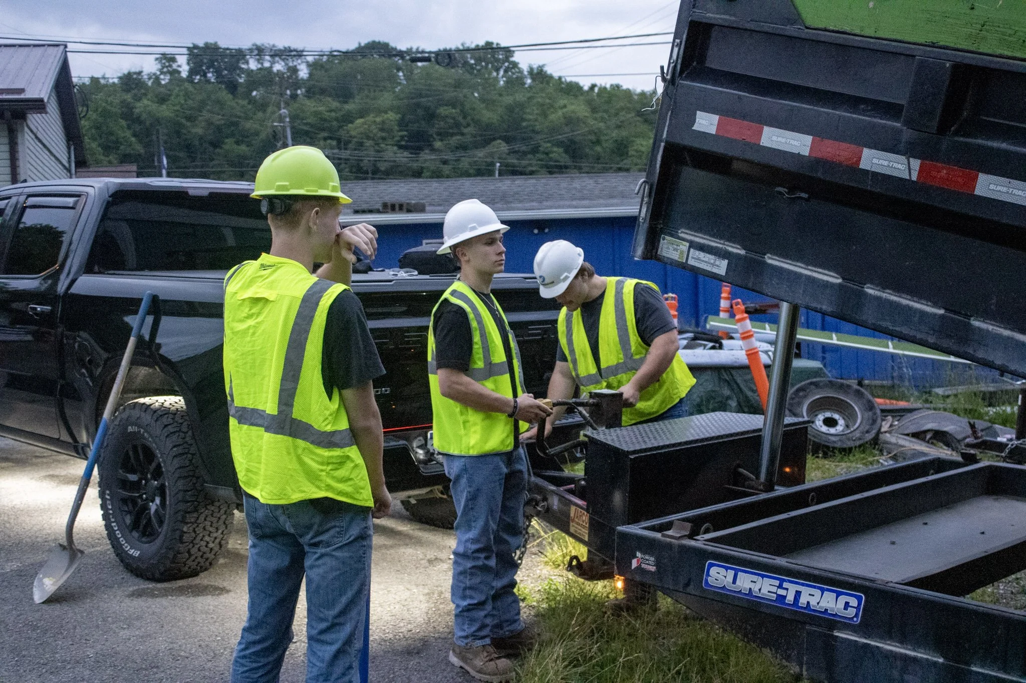 Three Junktion employees wearing safety helmets and reflective vests inspecting equipment outdoors near a black truck and demolition tools.