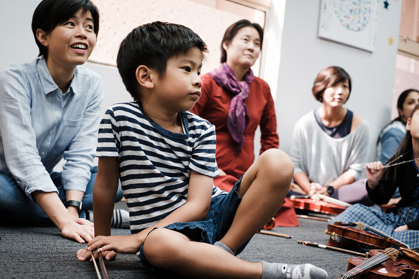 HKSMI Children and parents sitting on the floor at a music class with violins around them.