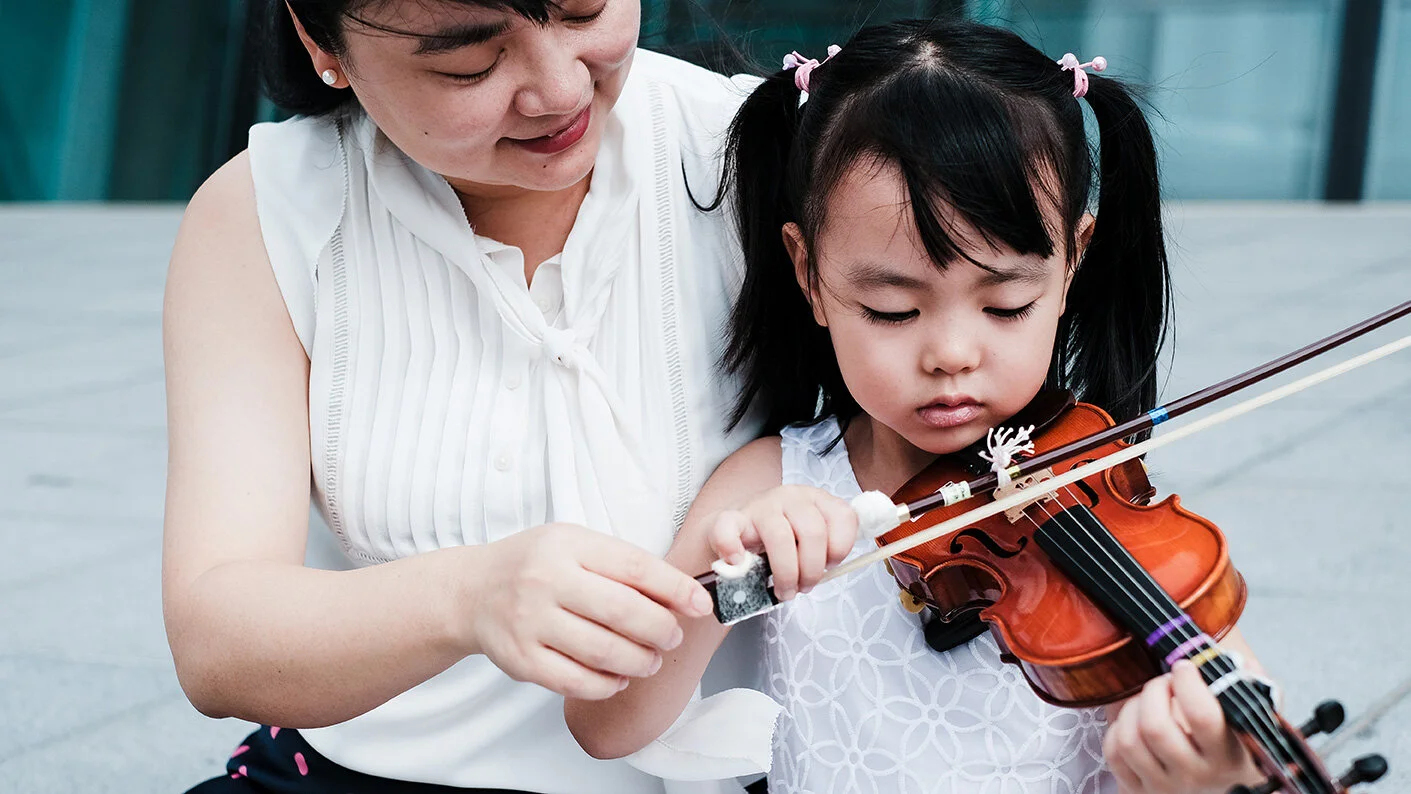 Young girl learning to play the violin with her parent's guidance