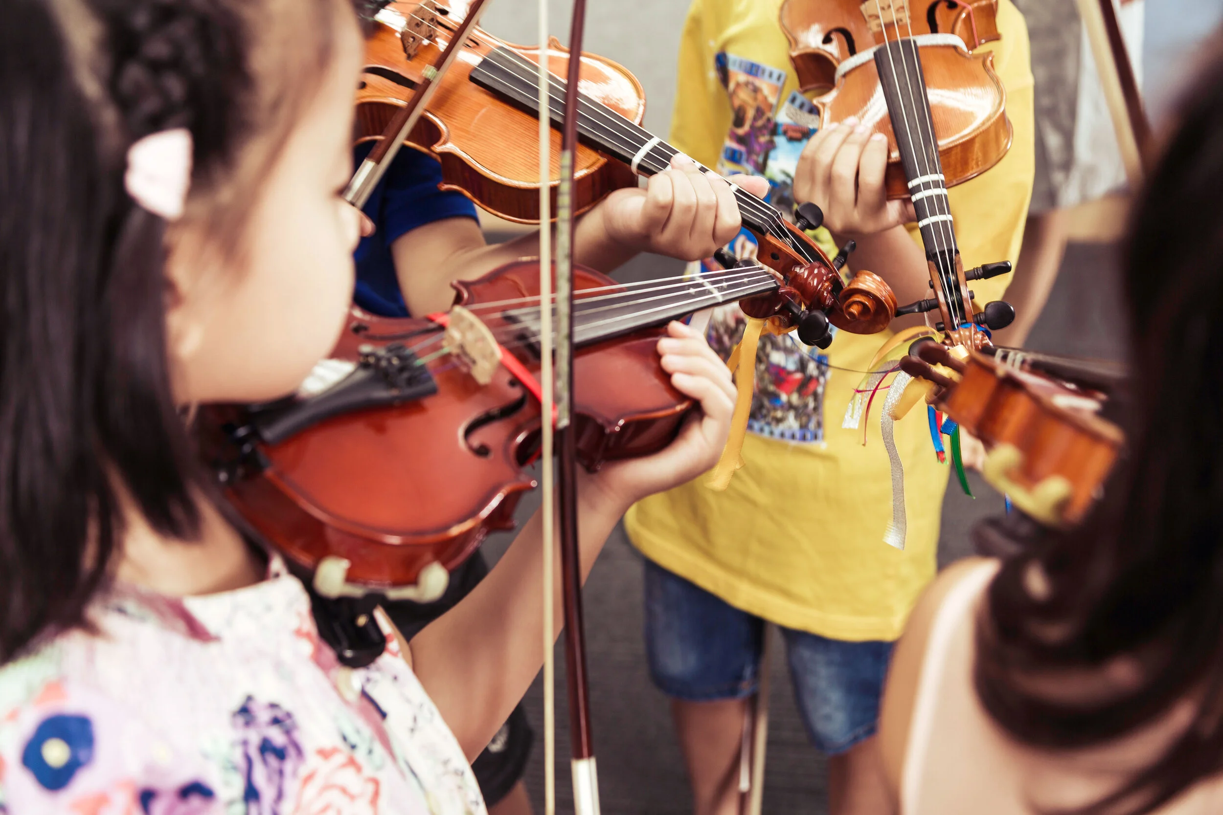 HKSMI Children playing violins in an outdoor setting.