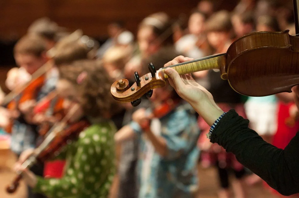 HKSMI Close-up of a person playing the violin with a group of children playing violins in the background.