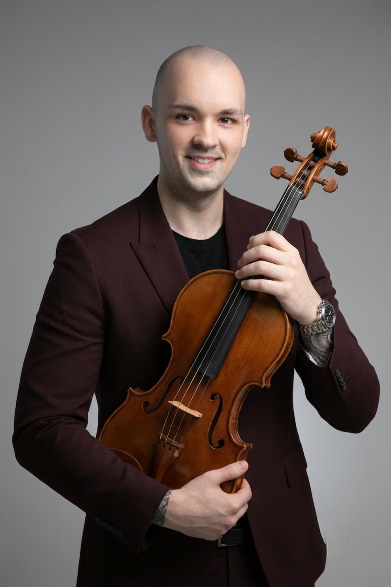 Mr. Evan Robinson: Portrait of a man holding a violin, wearing a dark blazer and smiling, against a plain background.