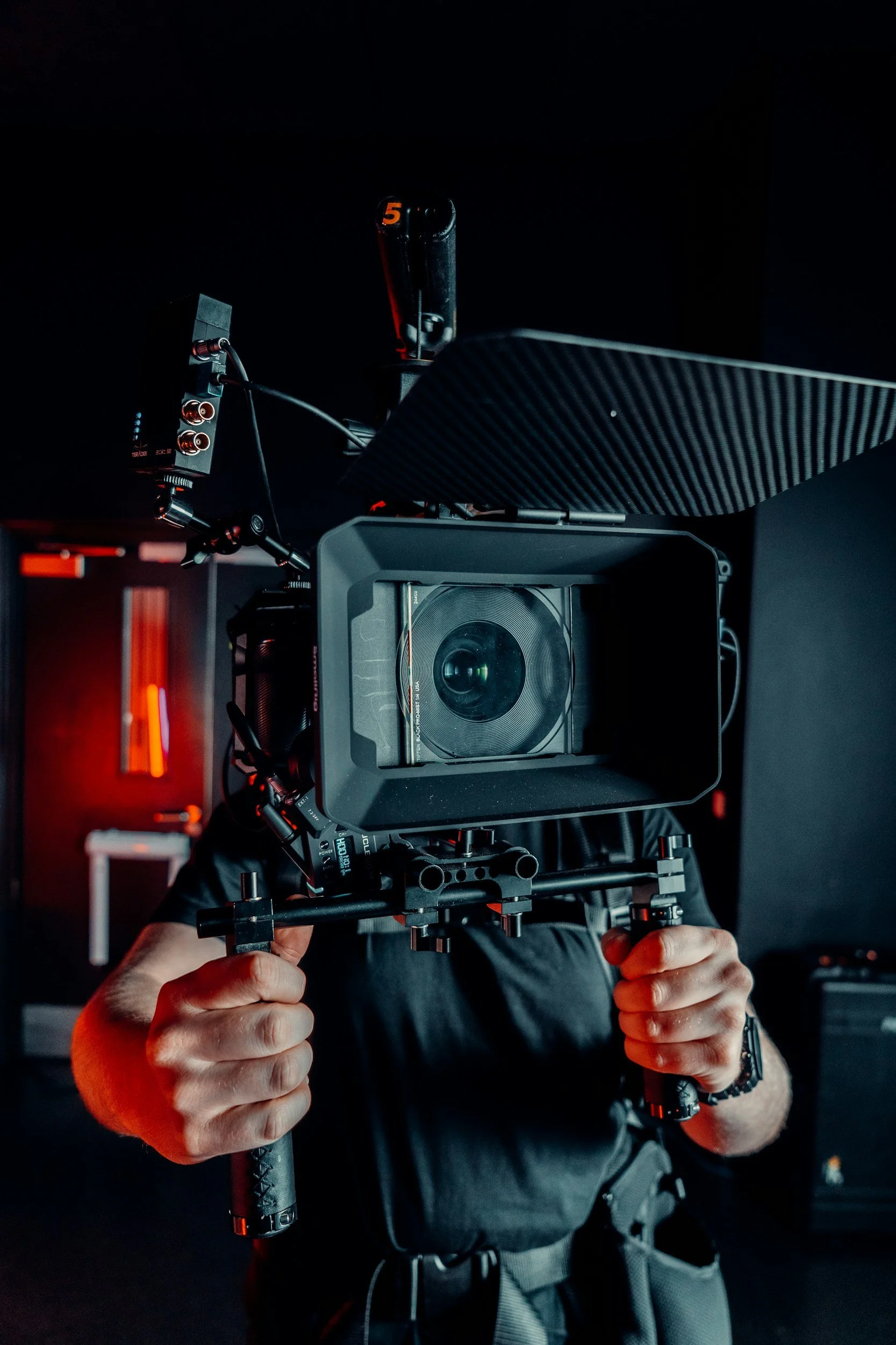 Person operating a professional camera on a stabilizer, with a dark background and red lighting accents.