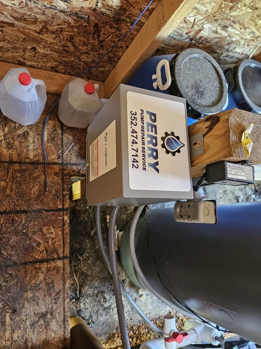 A pump repair service box on a wooden surface with plastic containers, a bucket, a stool, and some plumbing tools and hardware.