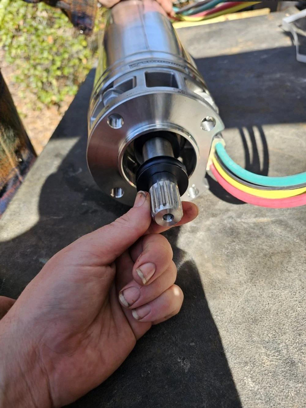 A person holding a metal motor with colorful wires connected to it on a workbench outdoors.