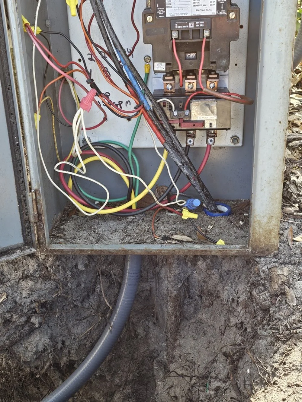 An open electrical box with various tangled wires and a large circuit breaker inside.