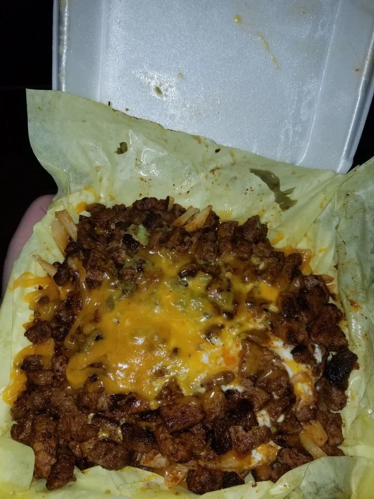 Open styrofoam food container with a baked dish consisting of ground meat, melted cheese, and onion on a sheet of paper or wax paper.