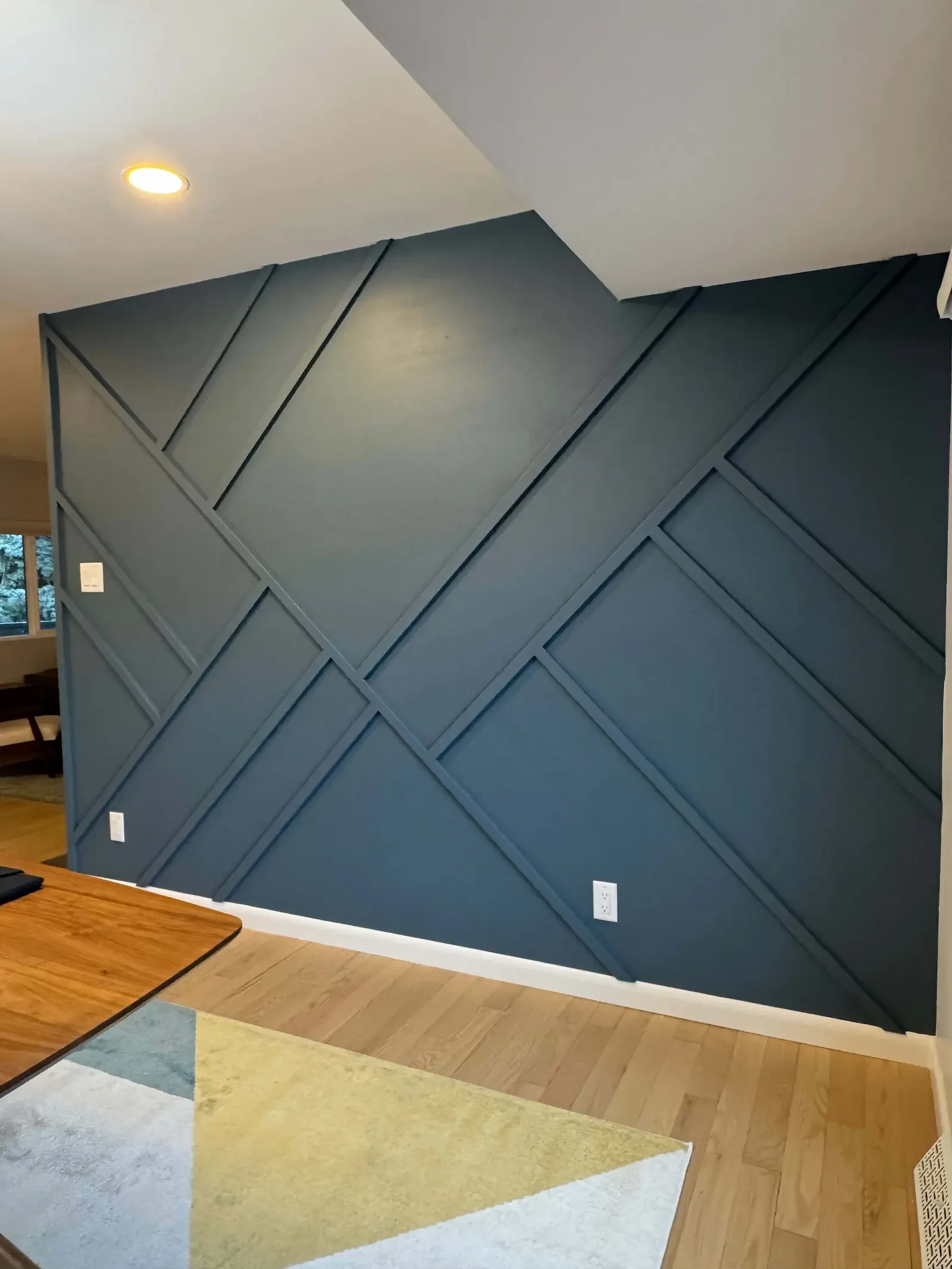 Simple geometric accent wall with angled trim pattern, soft neutral paint, natural light, and a modern entryway design.