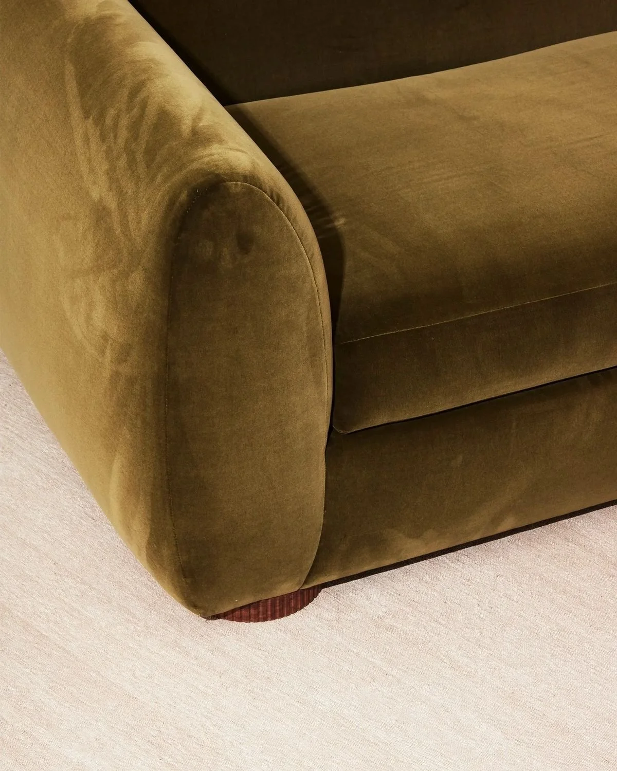 Close-up of a green velvet sofa with a curved armrest, seen from above, on a light-colored carpet.