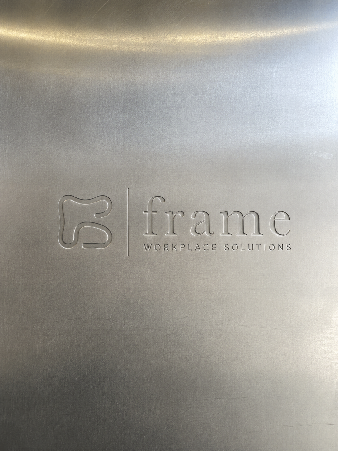 Close-up of a metallic surface with an embossed logo and text reading 'frame workplace solutions'.